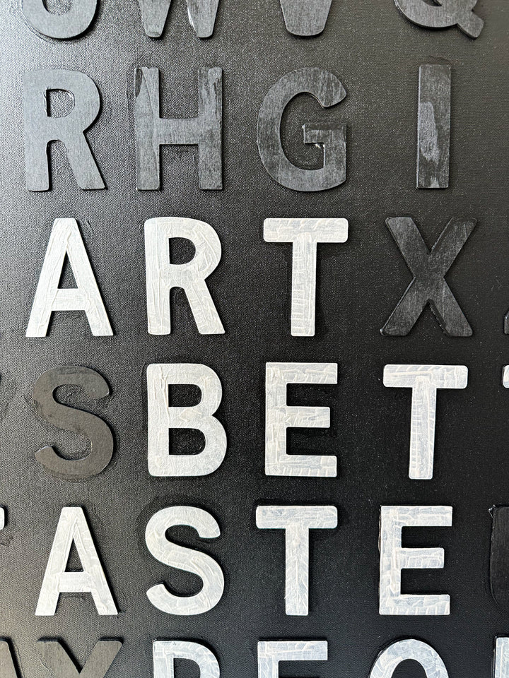 Steffanie Gerkin’s Have Good Taste Black 3D is a contemporary mixed-media typography artwork made with raised wood and acrylic letters on canvas, featuring a black monochrome alphabet grid with contrasting white letters that spell phrases including “Have Good Taste,” “Art,” “Better Taste,” and “People.”
