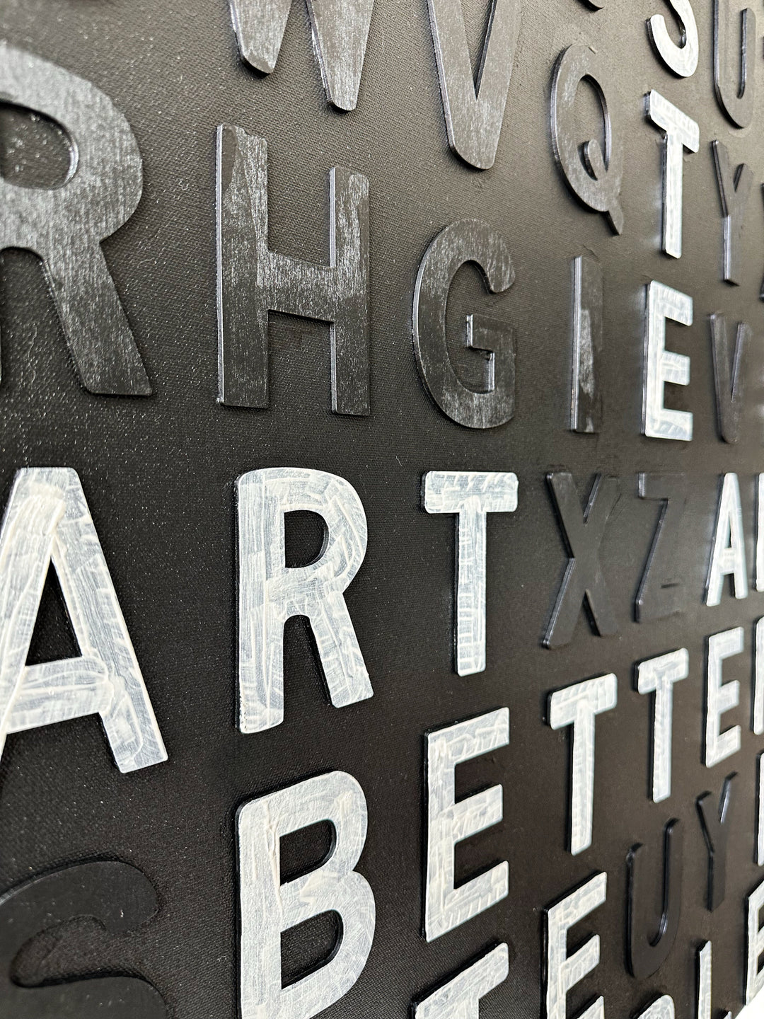 Steffanie Gerkin’s Have Good Taste Black 3D is a contemporary mixed-media typography artwork made with raised wood and acrylic letters on canvas, featuring a black monochrome alphabet grid with contrasting white letters that spell phrases including “Have Good Taste,” “Art,” “Better Taste,” and “People.”