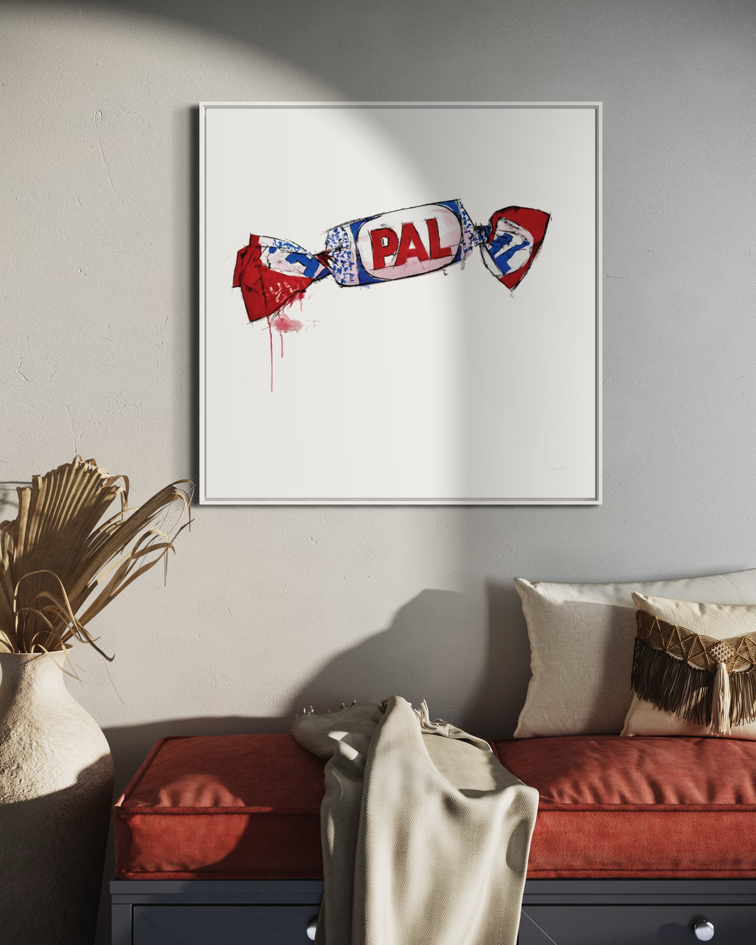 PAL framed in white hanging on wall above red couch with white pillow and blanket