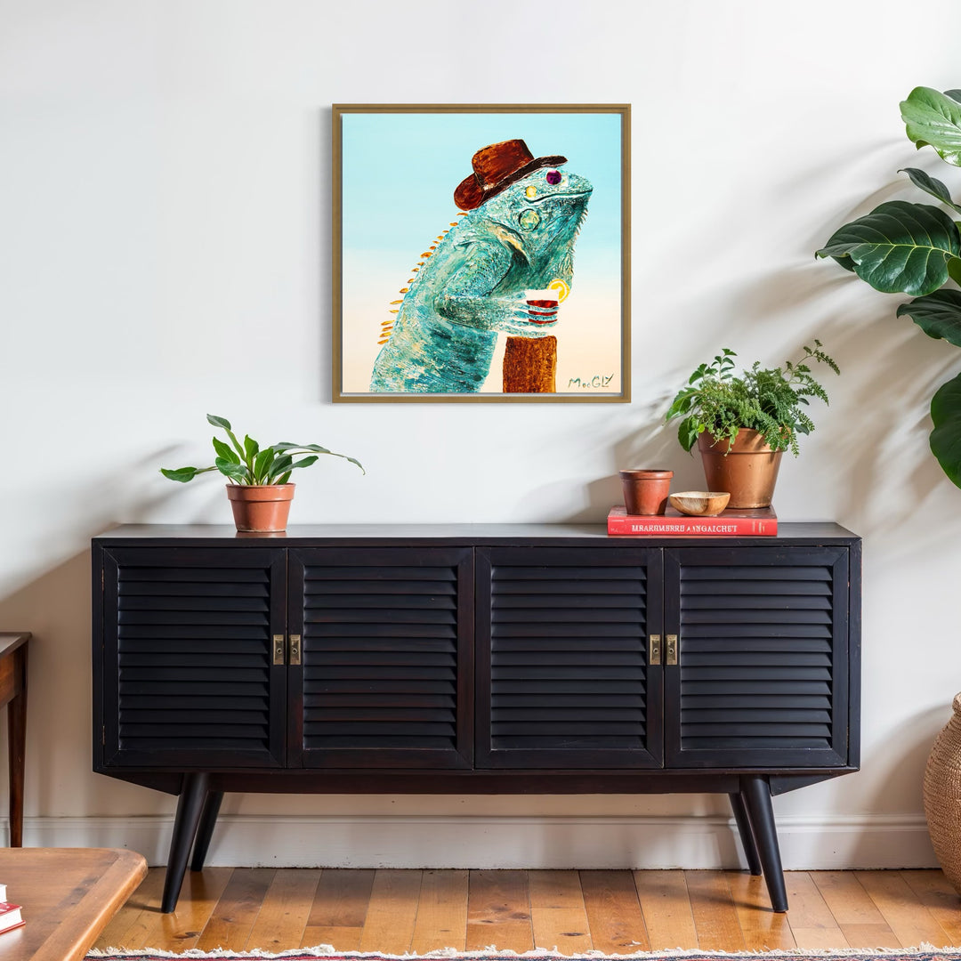 30” x 30” painting by French artist Moogly of a blueish-green iguana in sunglasses and a cowboy hat, holding a cocktail with a light blue background. The iguana is made out of resin, giving it a textured and shiny finish. The sunglasses are real round, reflective sunglasses that the artist has adhered to the canvas.