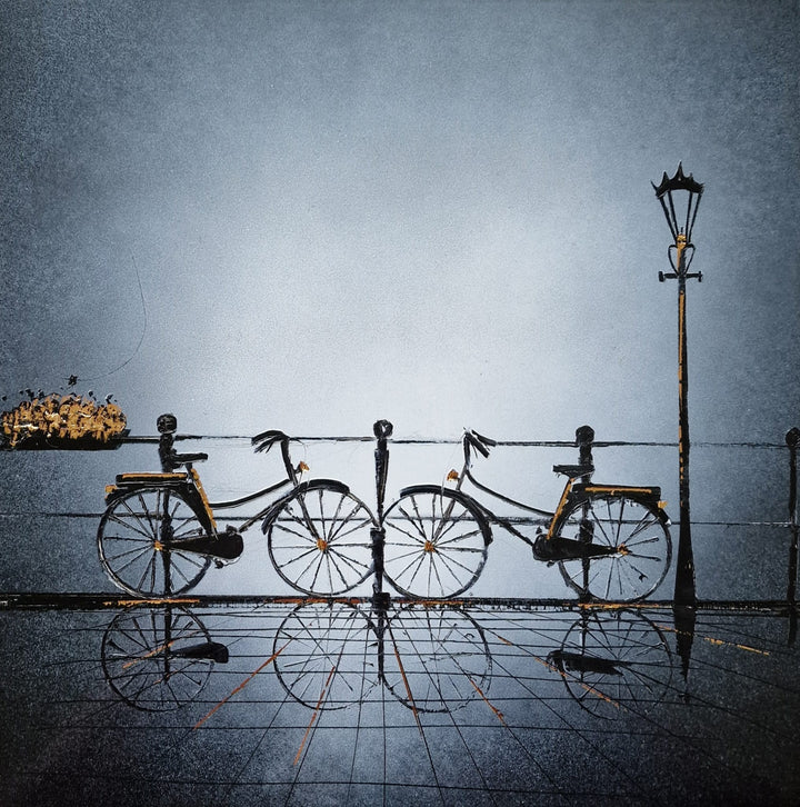 "Keep on Loving You" by French artist Julien Rey — a mixed-media painting of two bicycles on a rain-slicked Parisian quayside, crafted with Chinese lacquer and gold leaf on canvas. Two classic city bikes with gold leaf accents lean against a iron railing beside a tall street lamp, their reflections shimmering beautifully on the wet pavement below. A soft silver-gray sky evokes quiet romance and tender intimacy. Original contemporary romantic bicycle painting available at Morton Contemporary gallery.