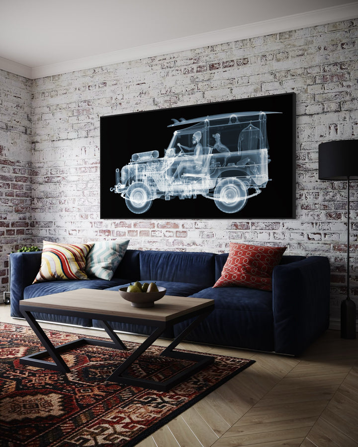 Framed Chromaluxe black and white x-ray photograph by Nick Veasey of a skeleton man driving a land rover with a surf board on the roof and a dog and surf suit in the back of the car. 