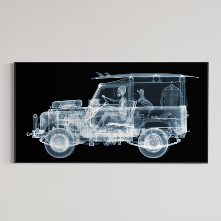 Framed Chromaluxe black and white x-ray photograph by Nick Veasey of a skeleton man driving a land rover with a surf board on the roof and a dog and surf suit in the back of the car. 