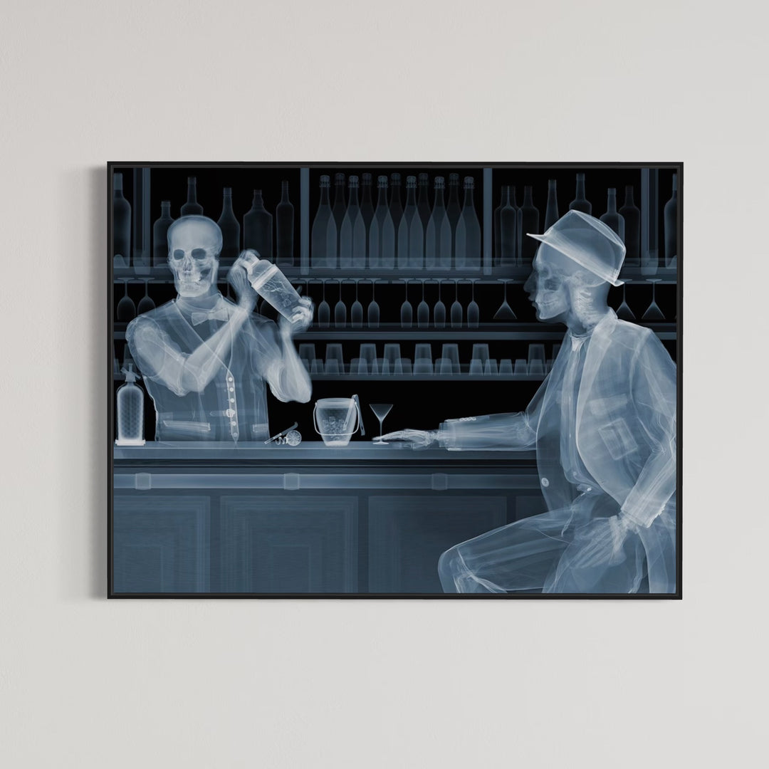 Framed Chromaluxe black and white x-ray photograph by Nick Veasey of two skeletons. A bar tender making a cocktail for a customer sitting at a bar with glasses and bottles behind them