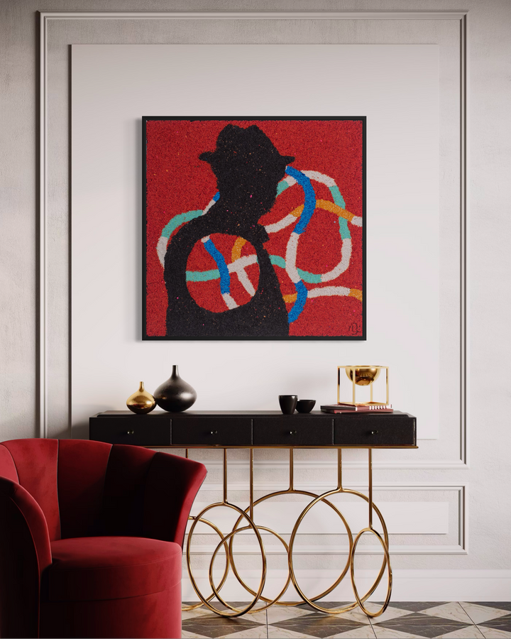 Bob Landstrom, Prism Postage, pigmented volcanic rock and acrylic on canvas, 20 x 20 inches. Black silhouette of a figure in a fedora hat with looping blue, teal, orange, and white lines on a red background, shown in a black frame above a black console table with gold ring legs beside a red velvet chair in a white paneled room.