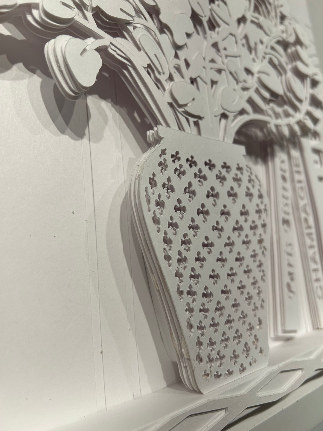 14"x14" layered white paper forming a vase with a fern over a wall.  